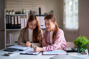 Two businesswomen in an office review documents together, smiling and focused, representing teamwork and productive collaboration in a formal business setting