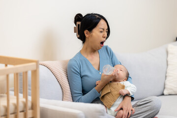 Tired mom feeding her newborn baby with milk bottle