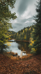 Fototapeta premium A serene lake surrounded by vibrant autumn trees under a moody sky, featuring a wooden dock extending into the water, capturing the beauty of nature in fall.