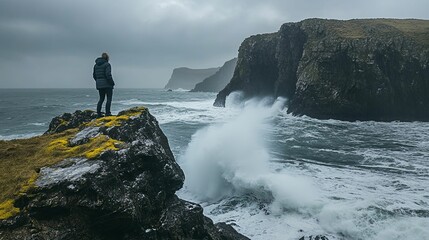 A lone figure stands on a cliff overlooking a stormy sea with crashing waves.