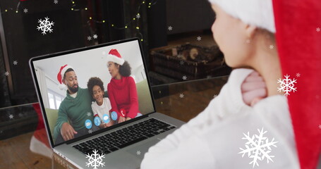 Image of snow falling over smiling woman in santa hat on laptop video call with her family