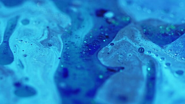 Sparkling fluid. Glitter oil drip. Defocused blue color shiny grain sequin particles water paint liquid pigment emulsion spill motion abstract art background.