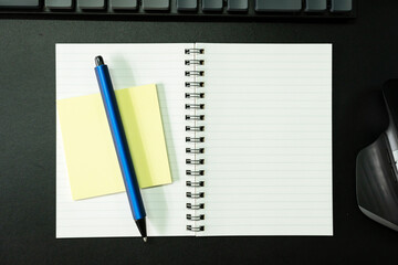 Top view of notebook. Blank paper notepad on office desk table with keyboard and other supplies. Blank notebook page for input the text. copy space, flat lay.