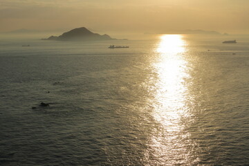 眩しい夕日に照らされる海面と大型船のシルエットと島影