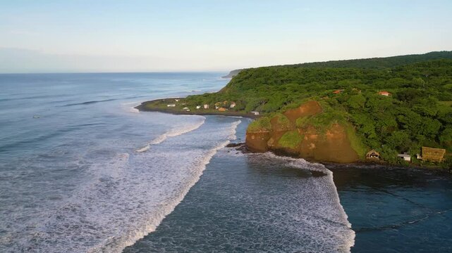 El Salvador beach aerial view of secluded surf spot of El Cuco called Punta Mango with cliffs, small huts and shacks and tranquil ocean setting - Dolly In