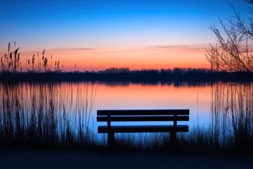 A lonely bench sits by a lake at dusk, the water reflecting the vibrant colors of the sunset.