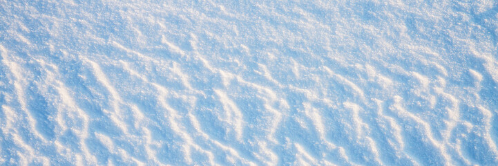 Beautiful winter background with snowy ground. Natural snow texture. Wind sculpted patterns on snow surface. Wide panoramic texture for background and design.
