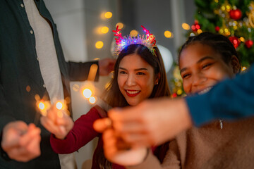 men and women holding sparkler fireworks in a party with Christmas tree. young couple Asian people enjoy celebrating Christmas and New Year. happy and celebrate with food wine and friendship for love,