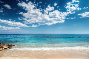 A serene beach with calm turquoise water and fluffy white clouds in a bright blue sky.
