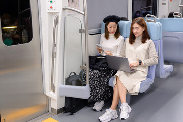 Two young Asian women collaborating on a laptop while traveling on a train, modern lifestyle and remote work concept.