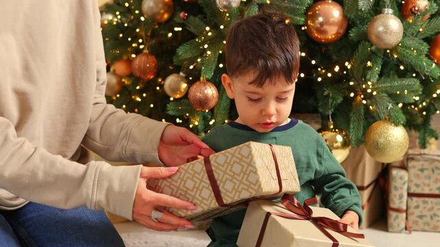 mother and son decorating christmas fir tree in cozy home interior.woman and boy kid putting globes balls on branch, playing covering eyes or unboxing gift.smiling female mom having fun with child.