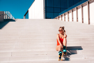 Young smiling blond model in summer swimwear red bathing suit. Sexy carefree woman having fun. Hot female posing in the street in sunny day. Cheerful and happy,  riding quad rollers, full length
