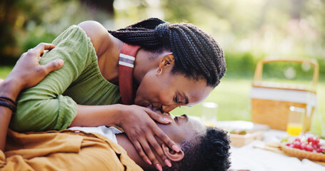Love, kiss and black couple at picnic in park for bonding, connection and outdoor adventure on happy weekend. Nature, man and woman on blanket for date together with romantic embrace, smile and trust