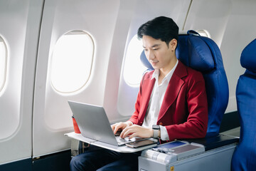 Young Asian executive excels in first class, multitasking with digital tablet, laptop and...