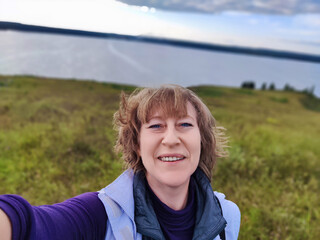 Woman blogger takes a joyful selfie by the serene lakeside during her latest travel adventure in nature