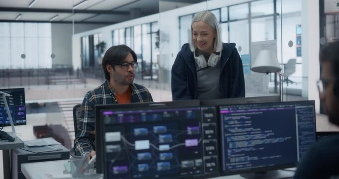 Two Young Colleagues Working on a Computer and Talking at a Workplace. Female and Male Software Developers Discussing a Solution for Their Collaborative Artificial Intelligence Project