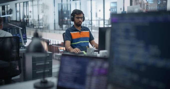 Focus Switching From a Computer Monitor with Software Code to a Portrait of a Thoughtful Engineer Behind a Desk in a Technological Corporate Office. Young Indian Man Using Headphones to Focus on Work