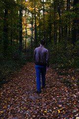 Young man in a brown leather jacket in an autumn forest