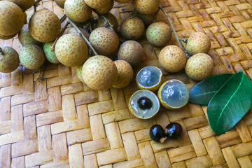 Bunch of fresh local longan fruit and peeled longan with leaves in bamboo basket isolated on brown background, Asian tropical fruit. Longan harvest in the garden