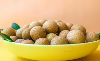 Fresh local longan fruit peeled with leaves in a plate on a yellow background, Asian tropical fruit. Longan harvest in the garden