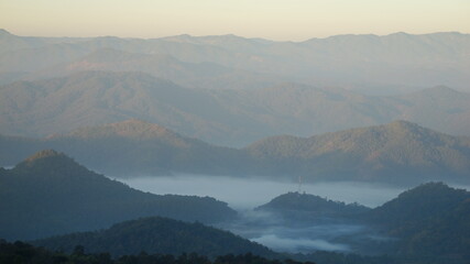 Landscape of layered mountains covered with a thin mist between the valleys, either in the morning or evening.