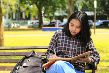 beautiful asian young woman college student focused writing on notebook and reading book in outdoors city park