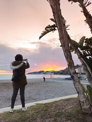 Souvenir from Almuñecar, tourist photographing the sunset on San Cristobal beach, Granada coast,...