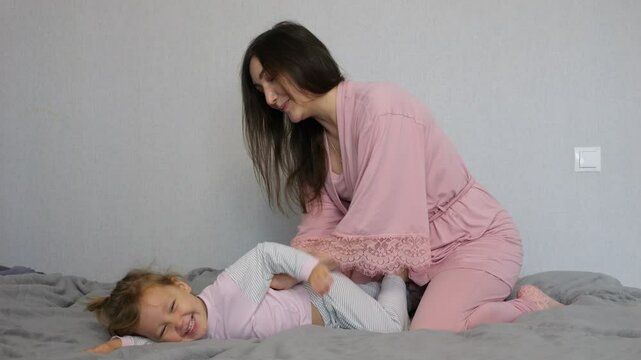 Joyful moments unfold as a mother tickles her daughter playfully on a cozy bed