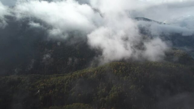 Le drone sort des nuages face &agrave; une montagne majestueuse verte et ses colines, aux sommets entour&eacute;s de brume.