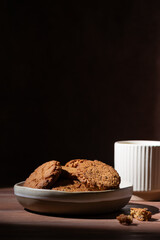 Cookie made of oatmeal and tea cup on a wooden table. Hard light. Vertical orientation.