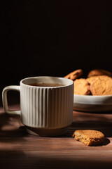 Cup of tea with oatmeal cookies in the plate on a wooden table. Hard light. Vertical orientation. Drink and homemade goods concept.