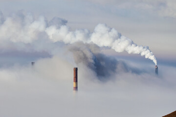 Smoke billows from industrial chimneys obscured by fog in a remote area during early morning hours