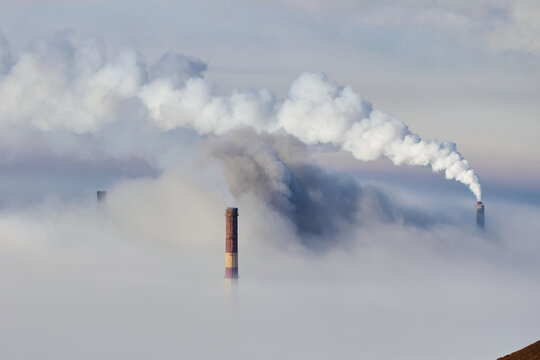 Smoke billows from industrial chimneys obscured by fog in a remote area during early morning hours