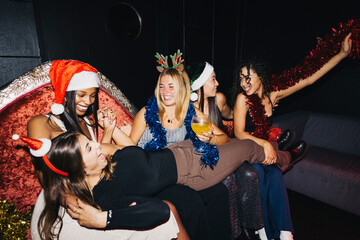 A group of friends enjoying a lively Christmas party in a night club, wearing holiday hats and...