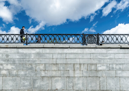 A man walks across a bridge against the sky.