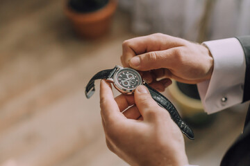 A man is holding a watch and looking at it. The watch is black and has a silver band