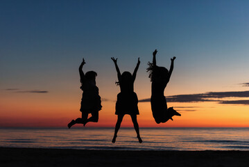 Women celebrate friendship by jumping on beach at sunset
