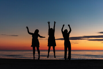 Silhouette of three girlfriends jumping on the beach at sunset