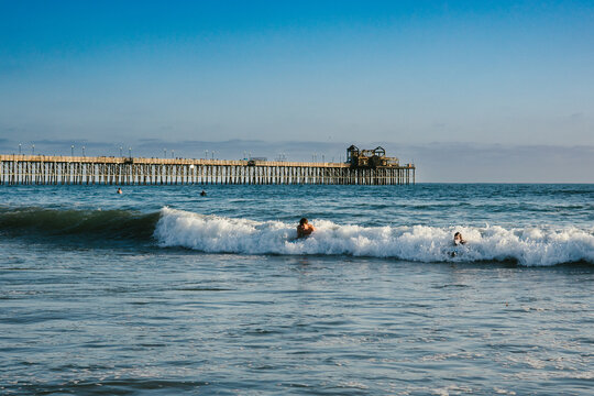 Siblings catch wave together on boards in ocean with pier