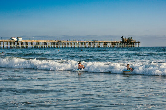 Family rides waves together in ocean in front of pier in summer