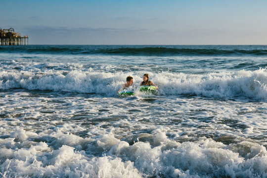 Siblings together happy riding boogie boards on waves in ocean