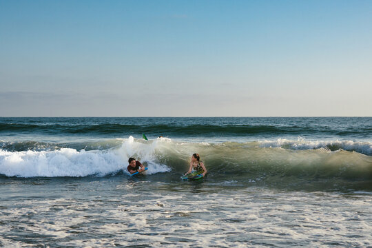 Boy and girl catch ocean wave on body boards with blue summer sky