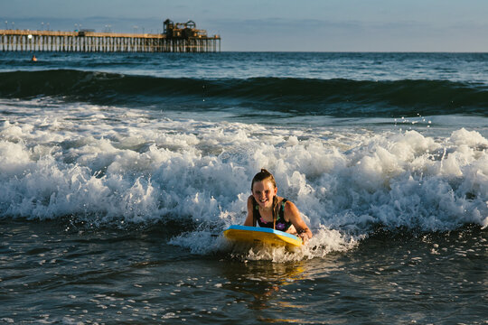 Girl laughs while riding boogie board on waves in ocean