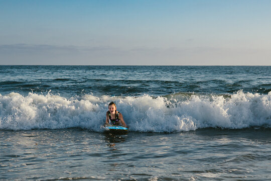 Girl laughs while riding wave on boogie board in blue ocean