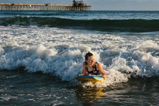 Girl body boarding in clear blue ocean looking towards the sun