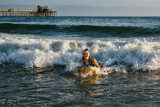 Girl laughs while riding boogie board on waves in ocean