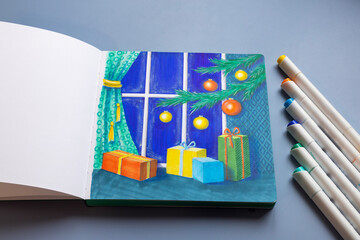 Drawing with markers in a sketchbook on the Christmas theme - a Christmas tree with decorations and gifts