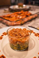 A glass bowl of food sits on a plate with a colorful pattern