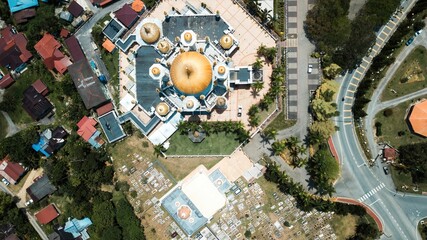 In a tropical setting, an aerial view of a mosque with golden domes encircled by homes and roads © Wirestock