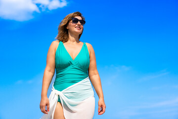 Summer vacation. Beautiful young woman in one-piece swimsuit and white sarong and sunglasses...